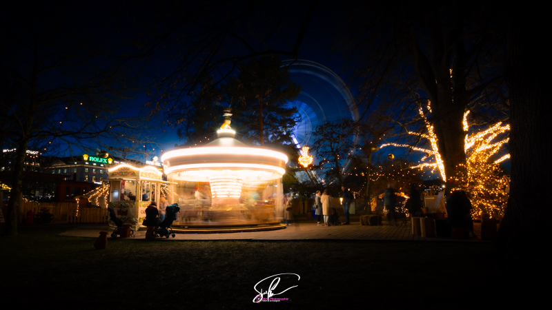 Photographie en pose longue du marche de noel de geneve dans le jardin anglais avec son manege et sa grande roue